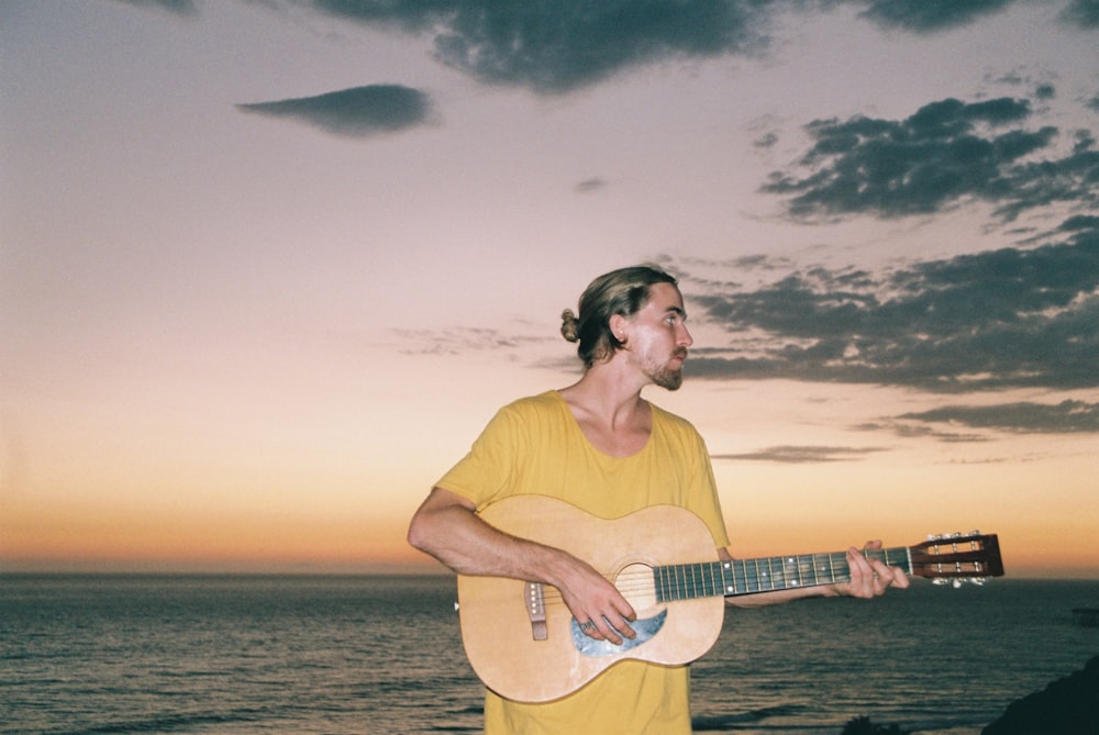 man wearing yellow crew-neck shirt playing brown acoustic guitar