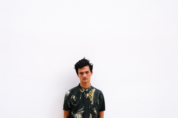 A person stands against a plain white background, wearing a dark shirt with an abstract, swirling pattern.