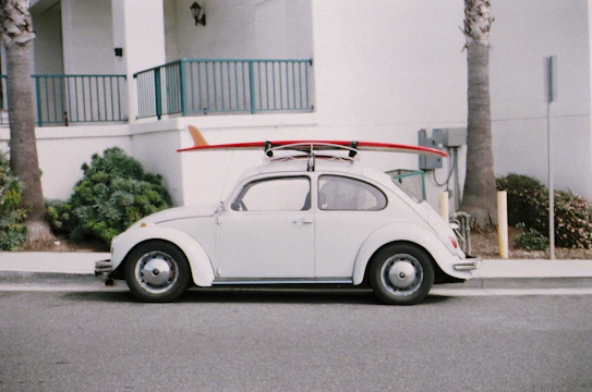 A customized Volkswagen Beetle painted in white, navy blue, and golden accents parked by the seaside.