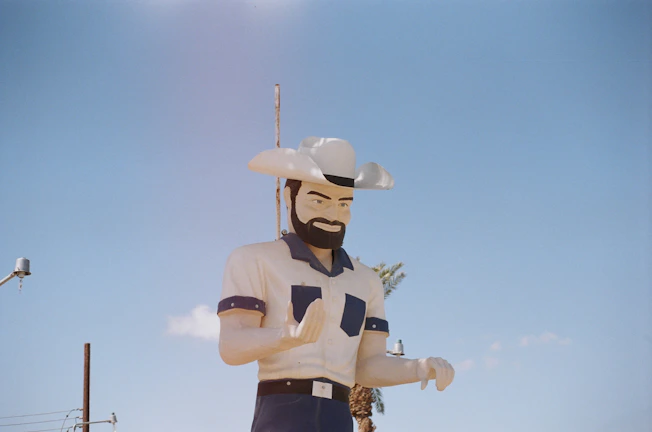 Tony of Tucson in rugged western attire, standing against a sunlit desert backdrop with his long white beard catching the light.