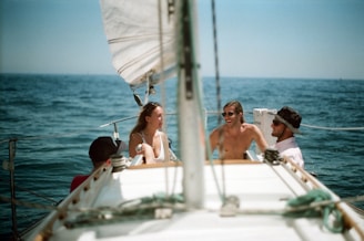 Crew members laughing and enjoying a sunny day on deck, with sails catching the wind.