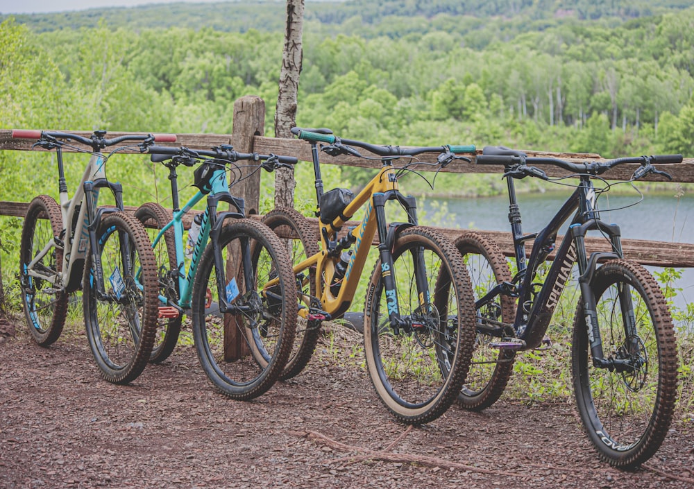 Cuatro bicicletas de montaña multicolores estacionadas junto a una barandilla de madera marrón