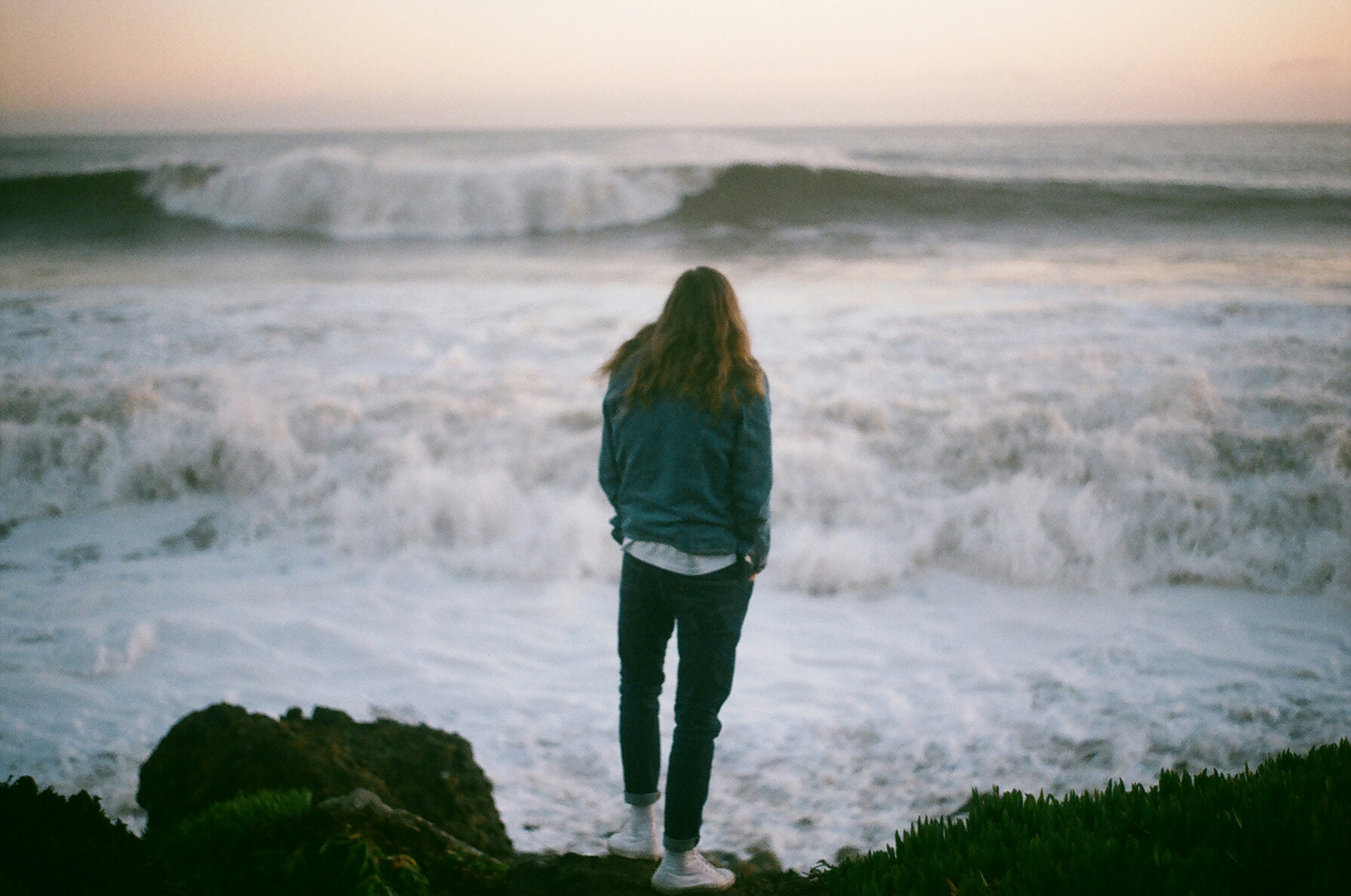 man in blue denim jacket and black denim jeans standing in beach