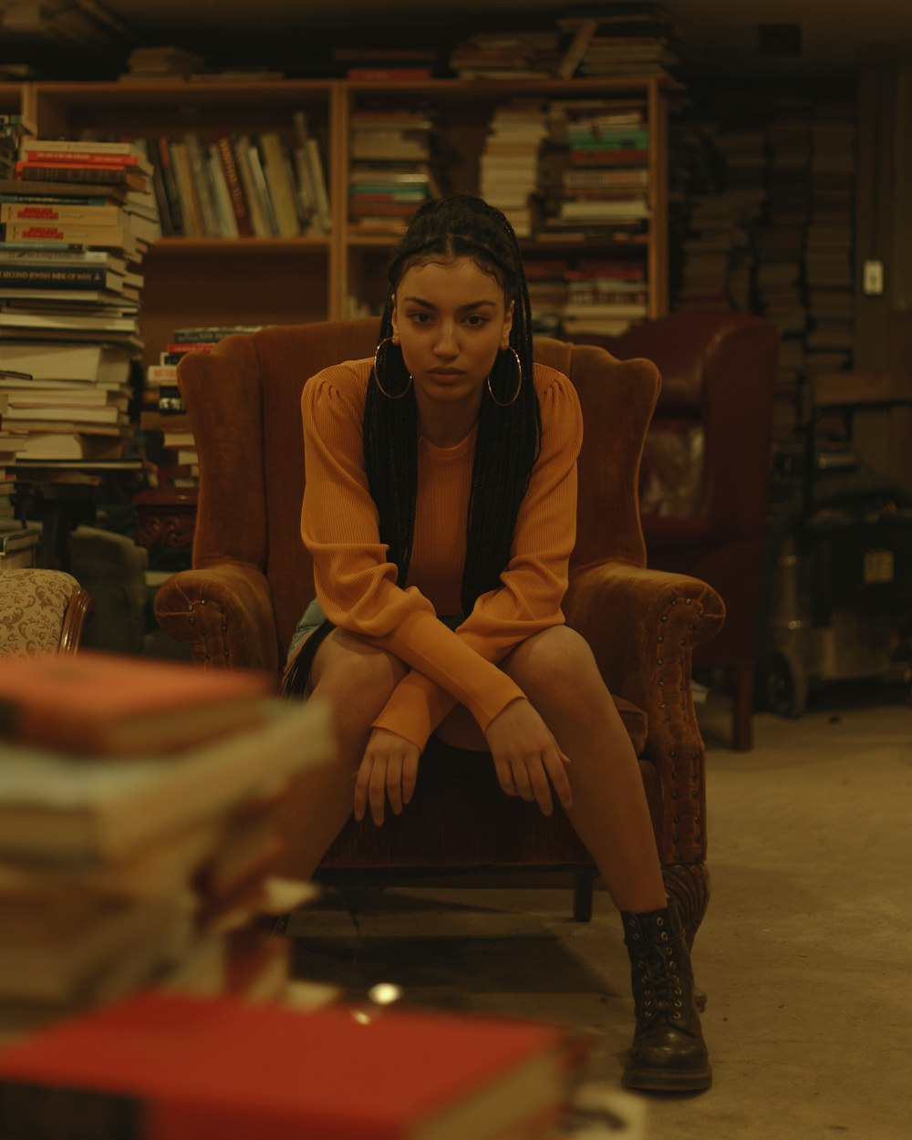 woman sitting on brown leather padded sofa chair in front of pile of books