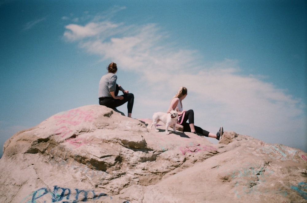 man and woman sitting on rock under white clouds