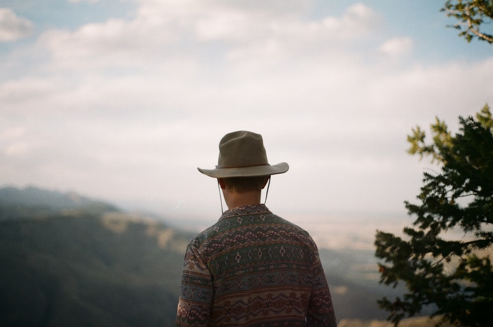 a man wearing a hat looking out over a valley
