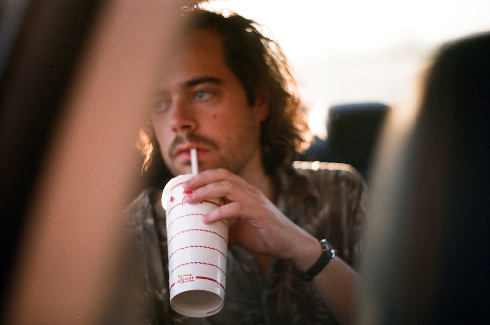 man in grey polo shirt drinking from white disposable cup in vehicle