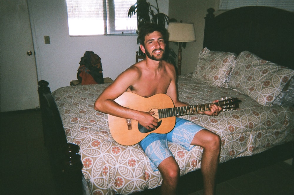 man sitting on bed while playing guitar