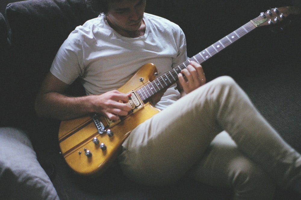 man sitting on sofa while playing guitar