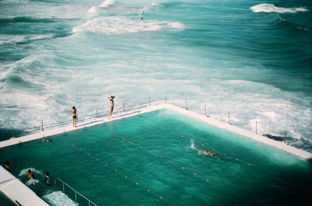 pessoas em pé e nadando na piscina ao lado do oceano