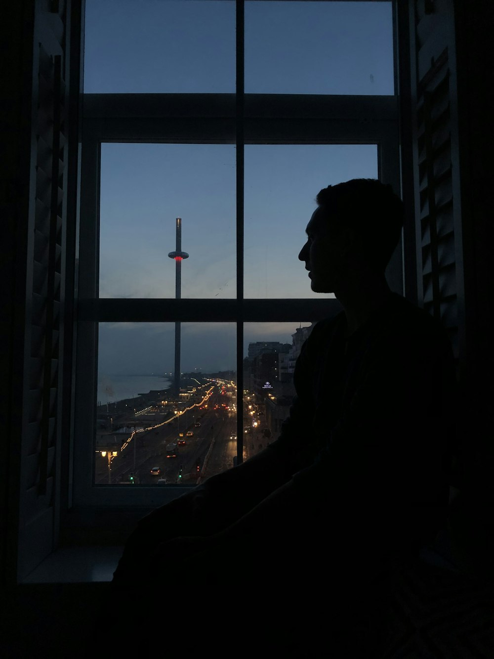 a man looking out a window at a city at night