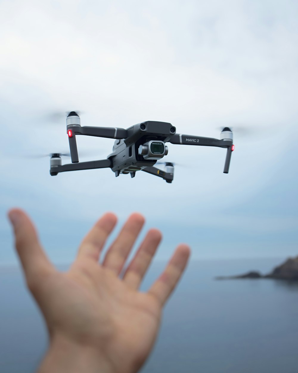 a hand holding a black and white remote control flying over a body of water