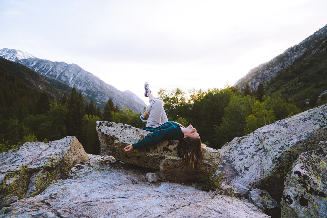 woman lying on big rock surrounded with tall and green trees