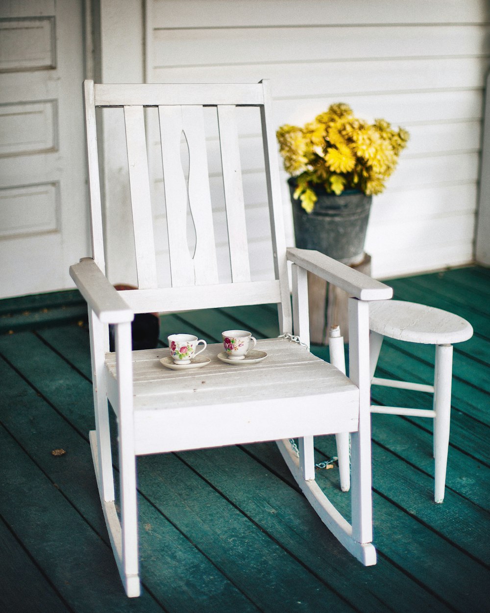 duas xícaras de chá de cerâmica floral branca e rosa e pires na cadeira de balanço de madeira branca
