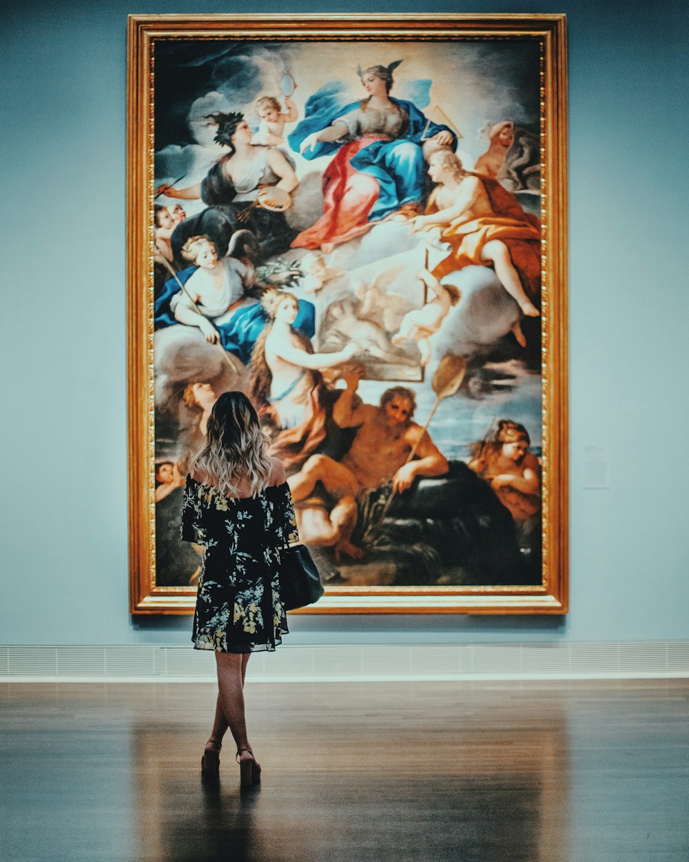 woman in black off-shoulder long sleeved mini dress standing in front of painting in museum