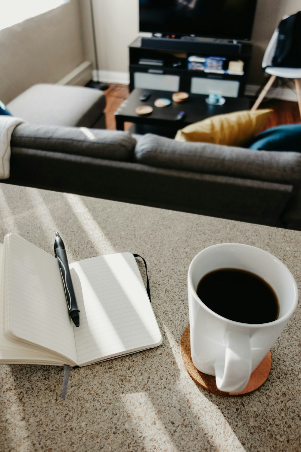 café negro en taza de cerámica cerca de bolígrafo de clic negro en la parte superior del cuaderno abierto