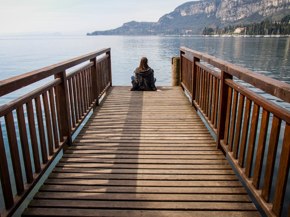 Persona che si siede sul molo di legno di fronte al mare