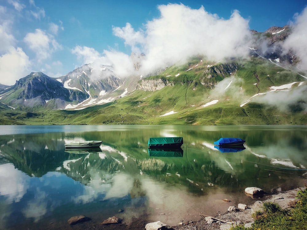 three white, green and blue boats on a lake