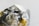 A close-up image of a raw, uncut gemstone or mineral with a rough texture and a multifaceted surface. The stone exhibits a mix of reflective and transparent qualities with metallic and earthy hues.