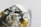 A close-up image of a raw, uncut gemstone or mineral with a rough texture and a multifaceted surface. The stone exhibits a mix of reflective and transparent qualities with metallic and earthy hues.