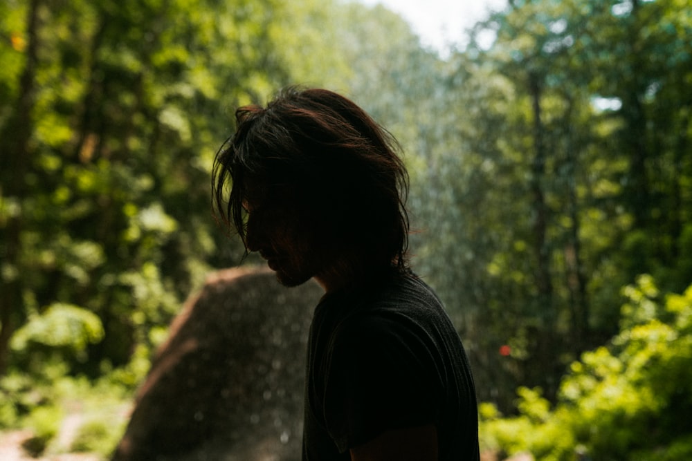 man standing and facing his right side surrounded with tall and green trees