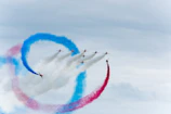 Dynamic airshow scene with planes performing synchronized maneuvers against a deep blue sky.