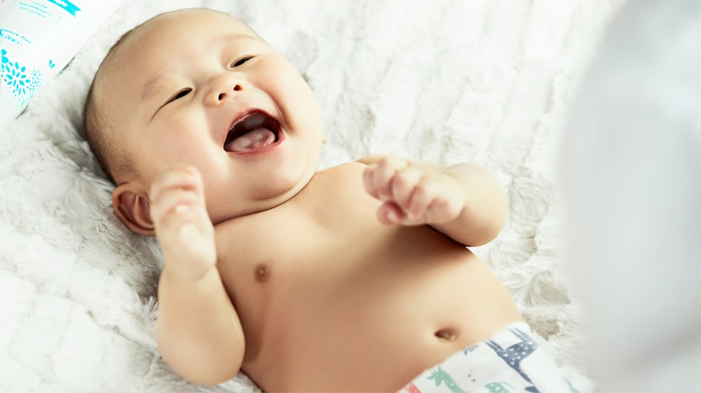 topless baby lying on bed smiling