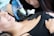 A tattoo artist in black gloves is focused on creating a tattoo on a client's upper chest area. The client, lying down with a slight smile, displays a sense of comfort. The tattoo machine is wrapped in a blue protective cover.