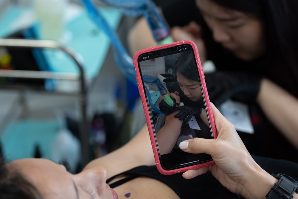 タトゥーマシンを持っている女性の黒いスマートフォンの話している写真を持っている人