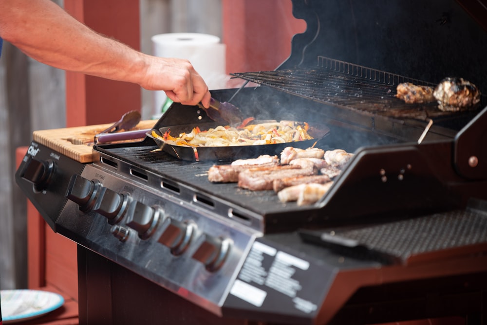 person grilling meats in gas grill