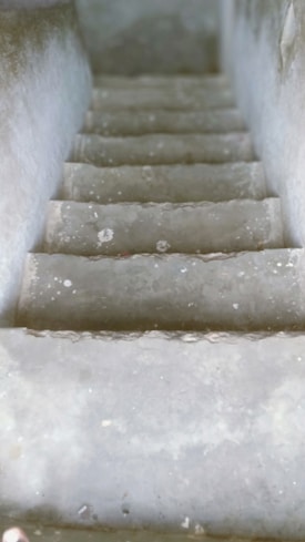 Concrete steps leading downward, surrounded by walls on both sides. The steps appear weathered and slightly narrow, with a visible texture on the surface.