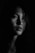 A person is captured in a moody, black and white portrait with dramatic lighting that highlights the face and expression.