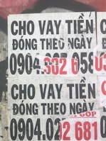 Several overlapping posters with bold text in Vietnamese advertising financial services. Some numbers are highlighted in red, indicating contact information. The posters are worn and layered on a rough urban surface.