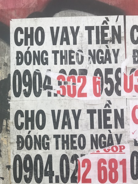 Several overlapping posters with bold text in Vietnamese advertising financial services. Some numbers are highlighted in red, indicating contact information. The posters are worn and layered on a rough urban surface.