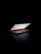 A slightly open laptop is positioned on a dark surface with a dark background. The screen displays a calm scene of the sky during sunset. The light from the screen casts a gentle glow around the laptop.