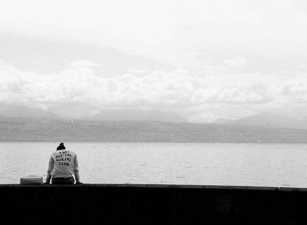 grayscale photo of person sitting across body of water