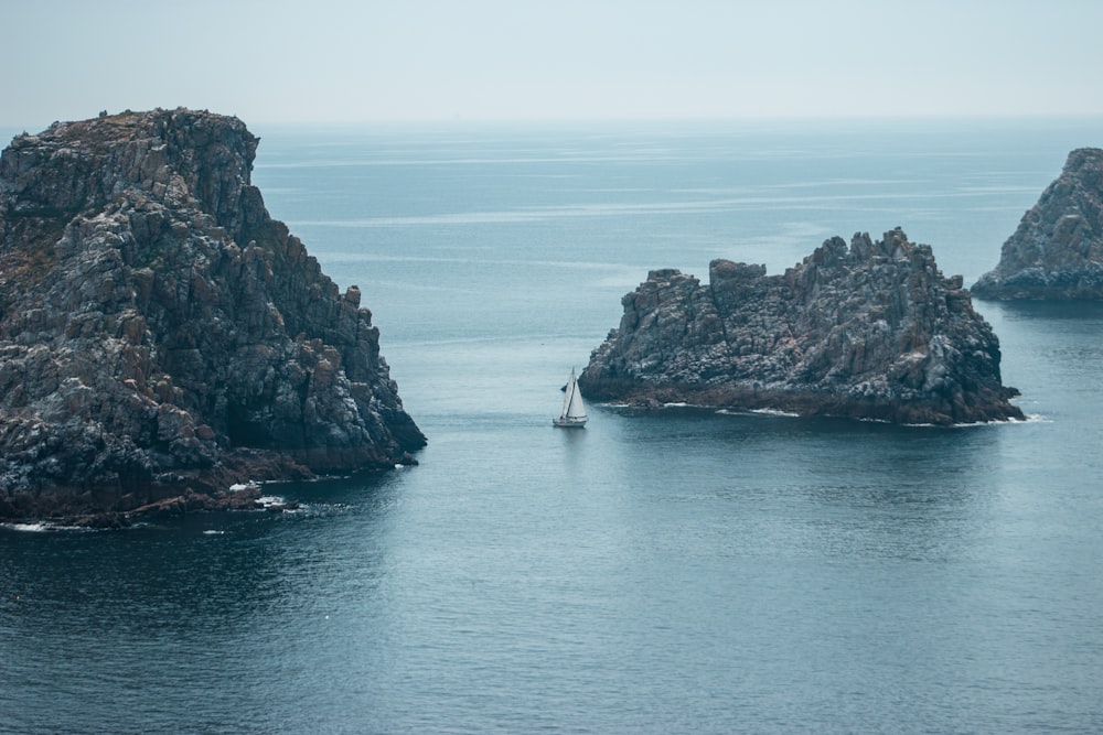 photography of white sailboat beside rock formation during daytime