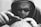 A person wearing a hood and sunglasses is intently focused on using a tool, possibly engraving or printing on a surface. The sunglasses have the words 'Chinatown Market' printed on them. The image is in black and white, emphasizing the details and textures.