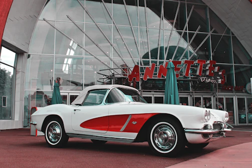 A vintage car parked beside a retro diner, with a model wearing a retrovibe jacket leaning on the hood.