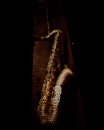 Dynamic shot of a wooden saxophone with dark shadows and orange highlights, set against a black backdrop with parallax effect.