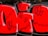 The image features a vibrant piece of graffiti art. Bold red and black colors create a striking visual impact. The design includes large, blocky letters with black outlines and smaller black doodles overlaid on the letters. The background is a dark wall, contributing to the vivid contrast.