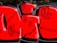 The image features a vibrant piece of graffiti art. Bold red and black colors create a striking visual impact. The design includes large, blocky letters with black outlines and smaller black doodles overlaid on the letters. The background is a dark wall, contributing to the vivid contrast.