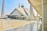 A large, modern mosque with a distinctive geometric design and a blend of traditional and contemporary architectural elements. Tall minarets flank the mosque, and there is a spacious courtyard with people walking around.