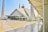 A large, modern mosque with a distinctive geometric design and a blend of traditional and contemporary architectural elements. Tall minarets flank the mosque, and there is a spacious courtyard with people walking around.