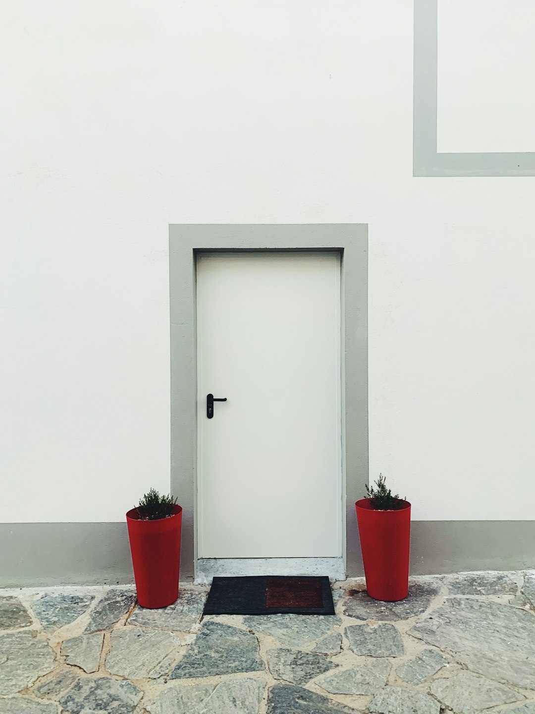 two red flower pots in both sided of closed red door