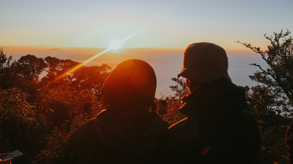 duas pessoas em terreno alto com vista para o mar durante o pôr do sol