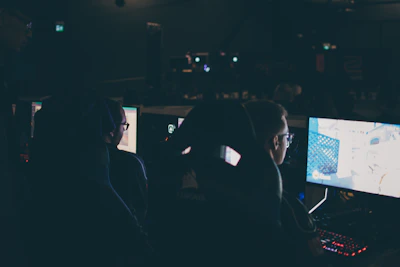 A group of gamers gathered around glowing monitors in a dimly lit room with blue ambient lighting.