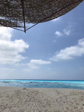 A serene beach with golden sand, turquoise water, and a red and yellow parasol swaying in the breeze.