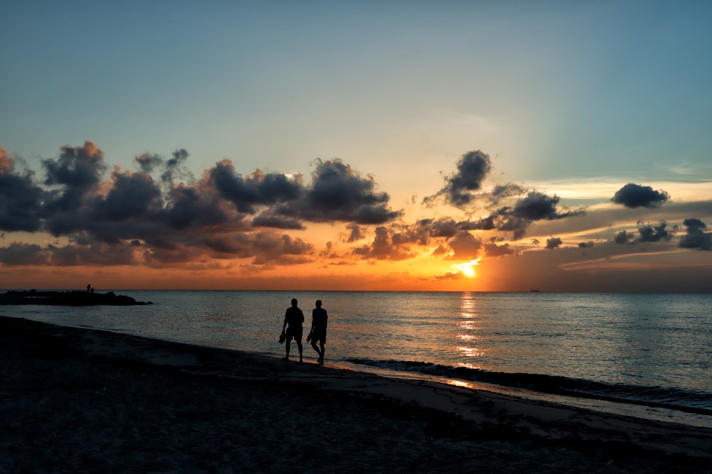 silhouette photography of two persons walking on beach line