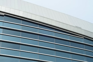 A modern architectural structure featuring a facade with large reflective windows and sleek metal paneling. The building has a curving roofline and the windows incorporate dark tinted glass, offering a sleek and contemporary appearance.